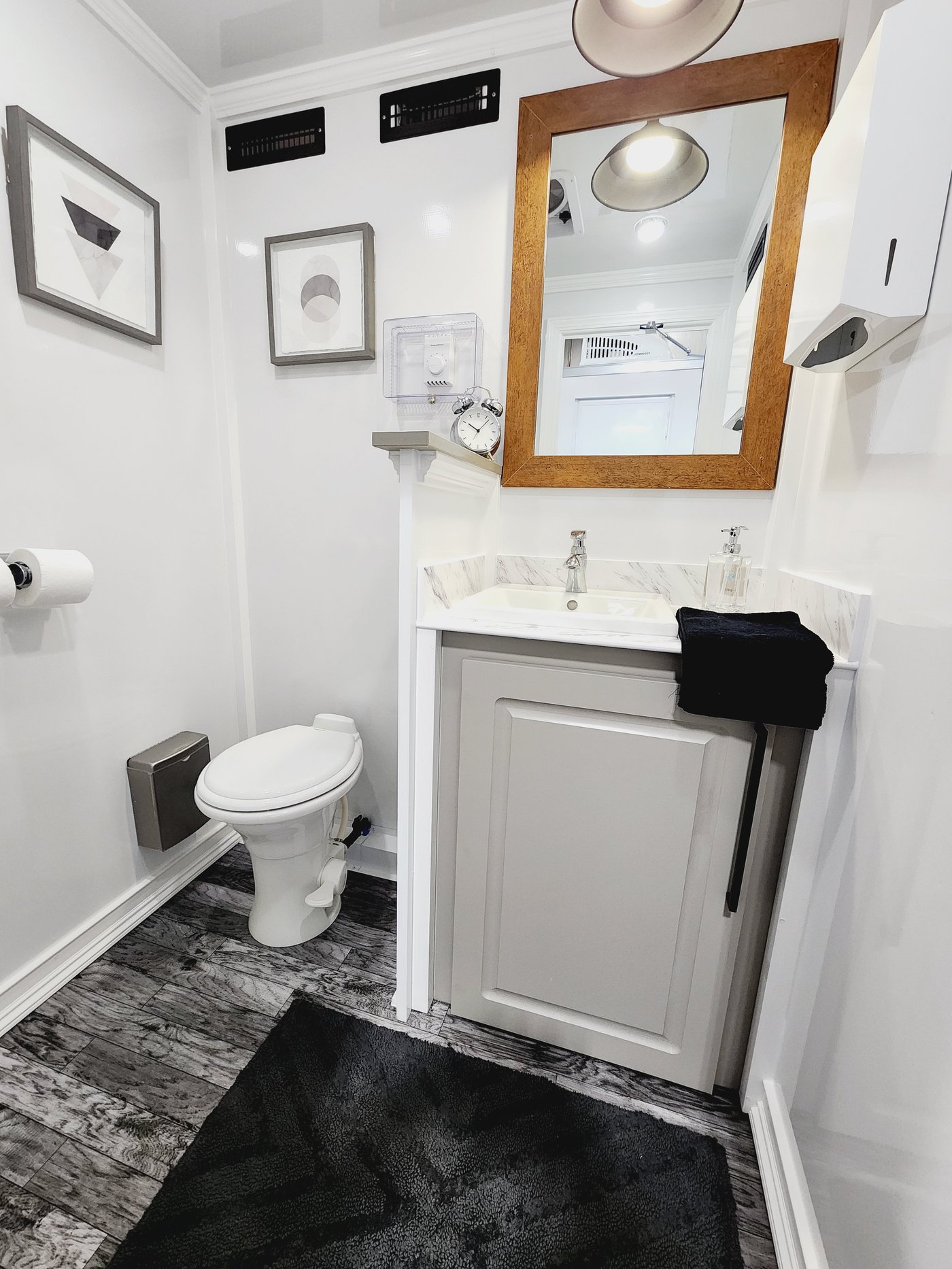 Luxury restroom trailer interior with wood-framed mirror, marble vanity, and chrome fixtures